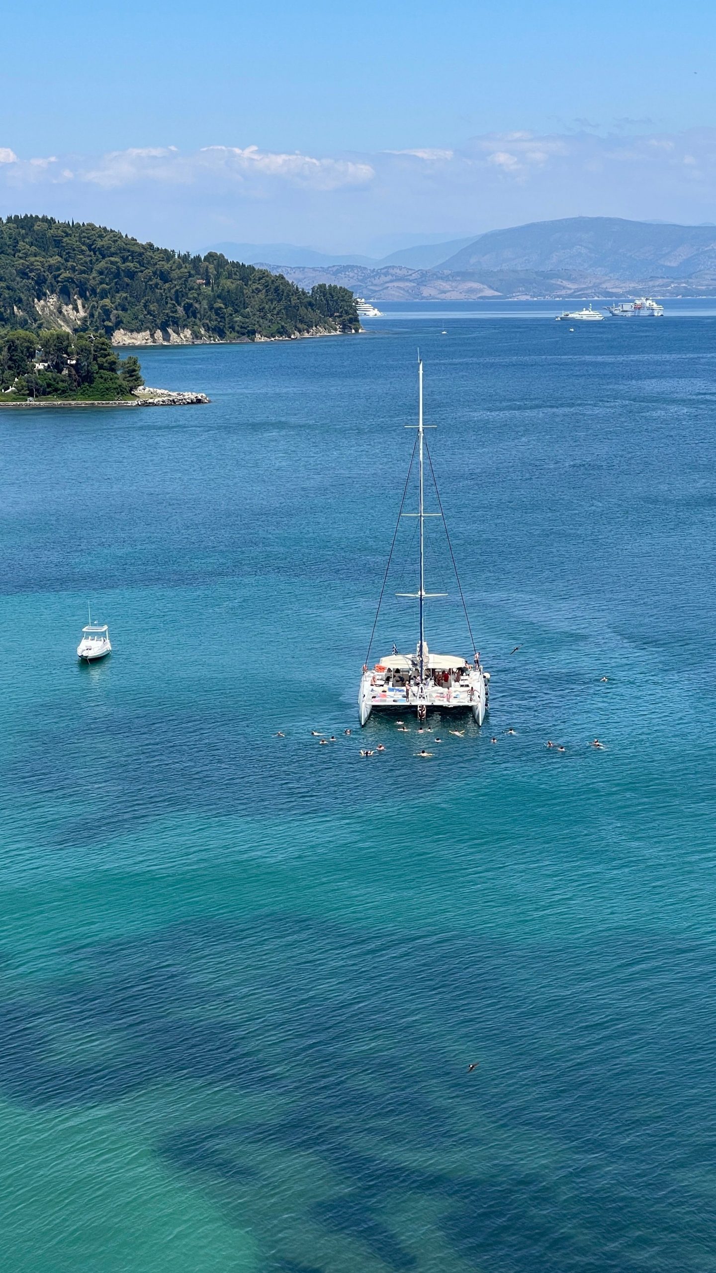 Stunning aerial view of catamaran and motorboat in crystal-clear sea near scenic coastline.