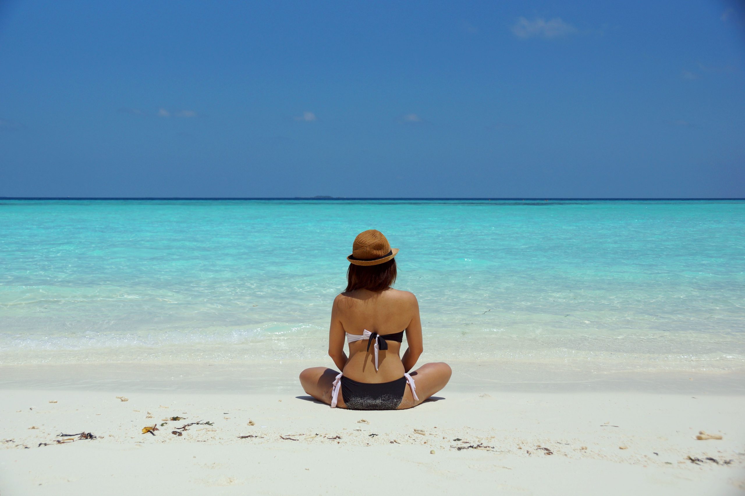 Rear view of a woman in a bikini and hat relaxing on a pristine beach in Maldives.